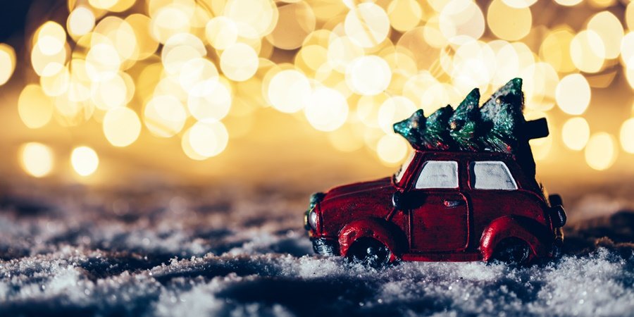 Red car with a Christmas tree driving through snowy road. Fairy lights, wintertime.