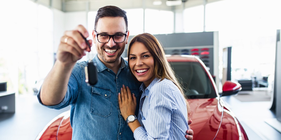 couple at a car dealership standing infront of a new car holding car key in one hand