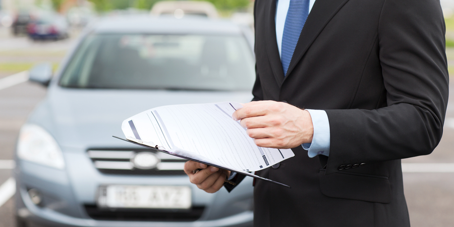 Well dressed man holding insurance papers in front of a car