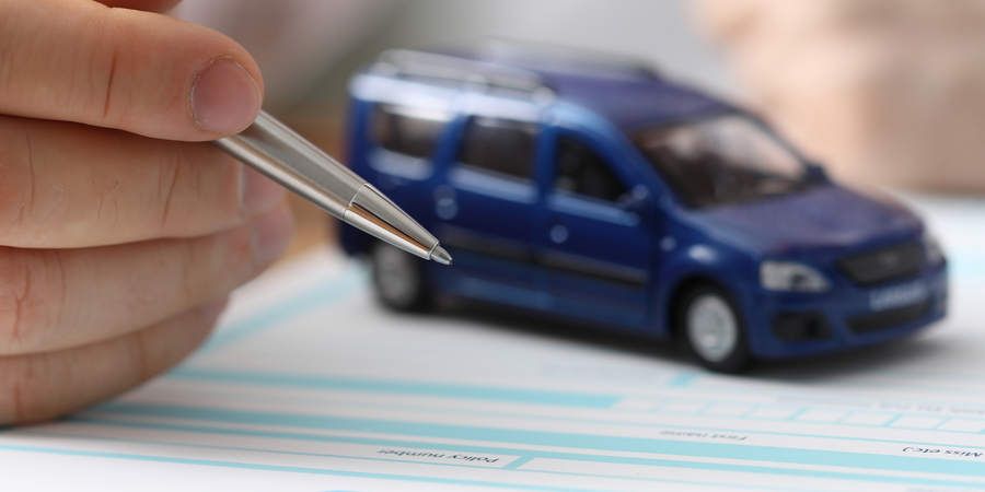 miniature blue SUV on top of an insurance policy and hand and pen ready