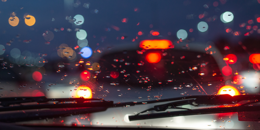 Looking through a wet car wind shield at night at the traffic lights of the cars