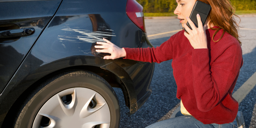 woman kneeling next to her damaged car calling insurance company