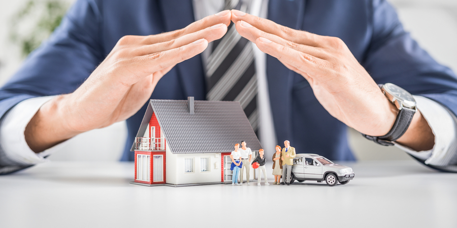 Business man using both hands as a roof to cover miniature house family and car