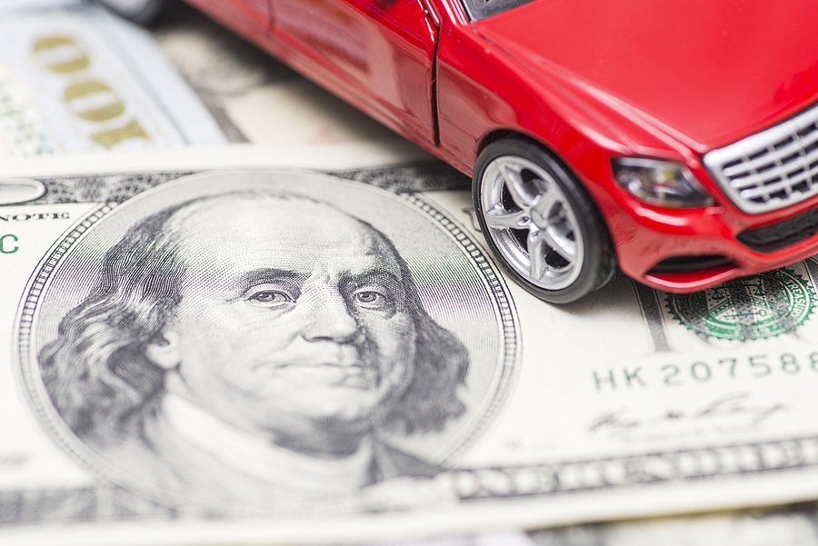 A replica small car laying on top of dollar bills