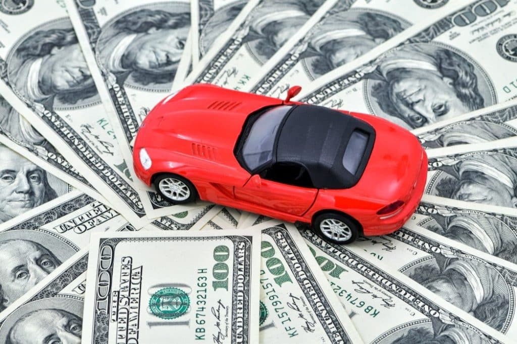 Replica red car laying on top of multiple hundred dollar bills