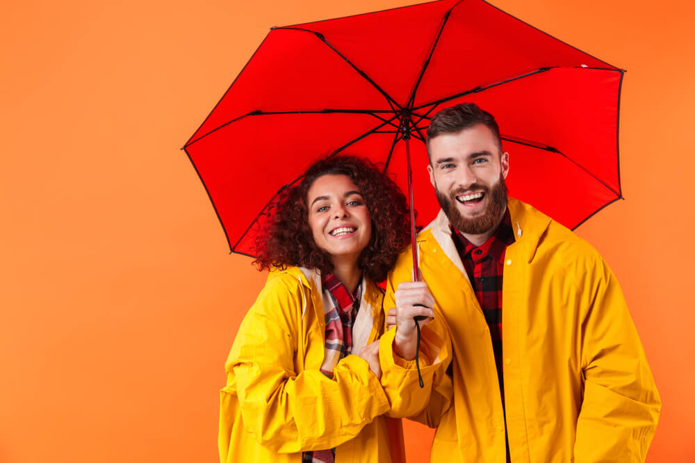 Couple wearing raincoats and holding umbrella representing a double protection against whatever comes their way