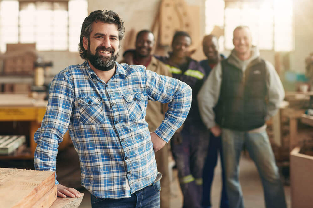 Business owner at workshop with employees standing proud and happy behind him