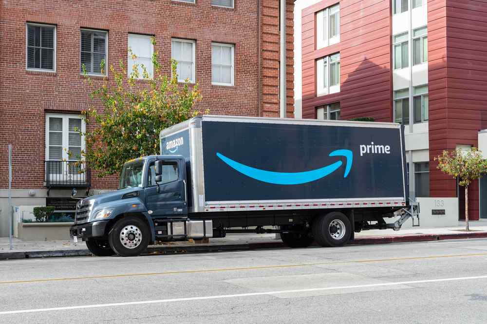 Box truck parked on the street with. a blue bent arrow drawn on its side in the shape of a smile. It is amazons prime logo.