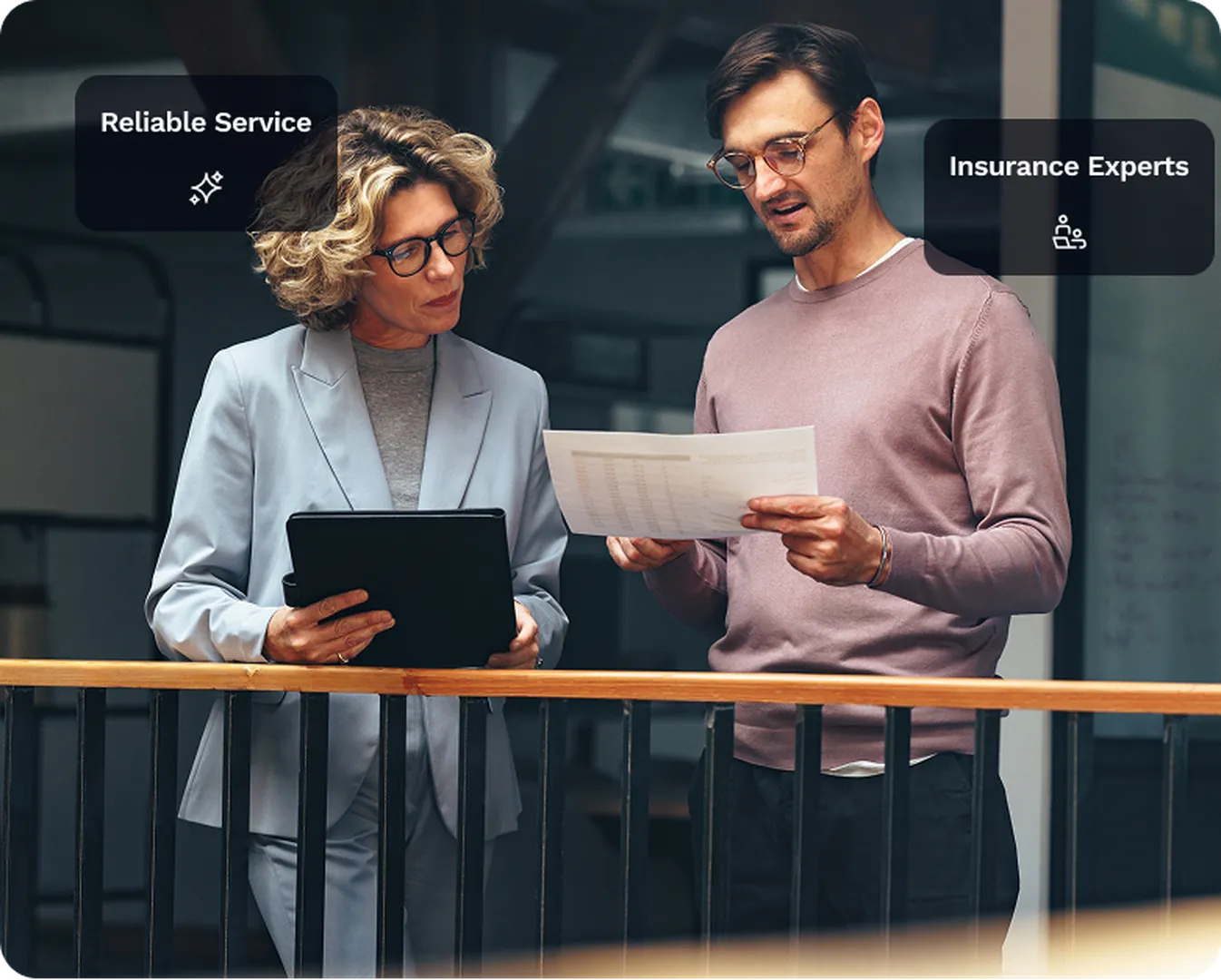 Two insurance experts, a woman and a man, review a document together in a modern office with 'Reliable Service' and 'Insurance Experts' badges.