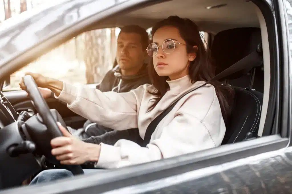 Young woman taking a driving test with the examiner seated beside her in the car.
