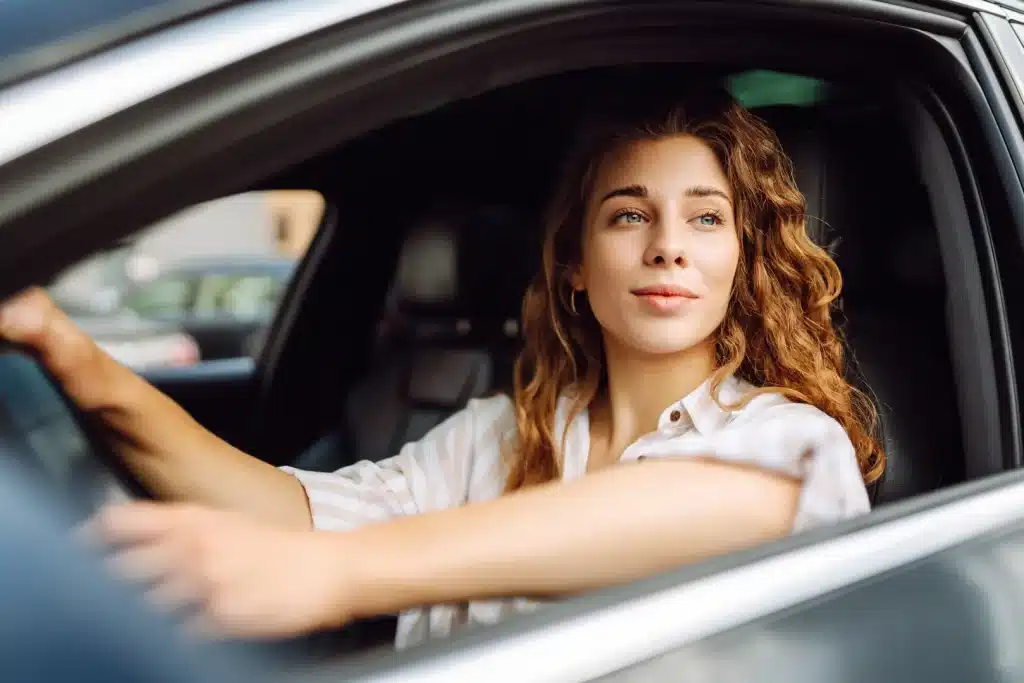 Woman with curly hair driving a car, looking out the window.