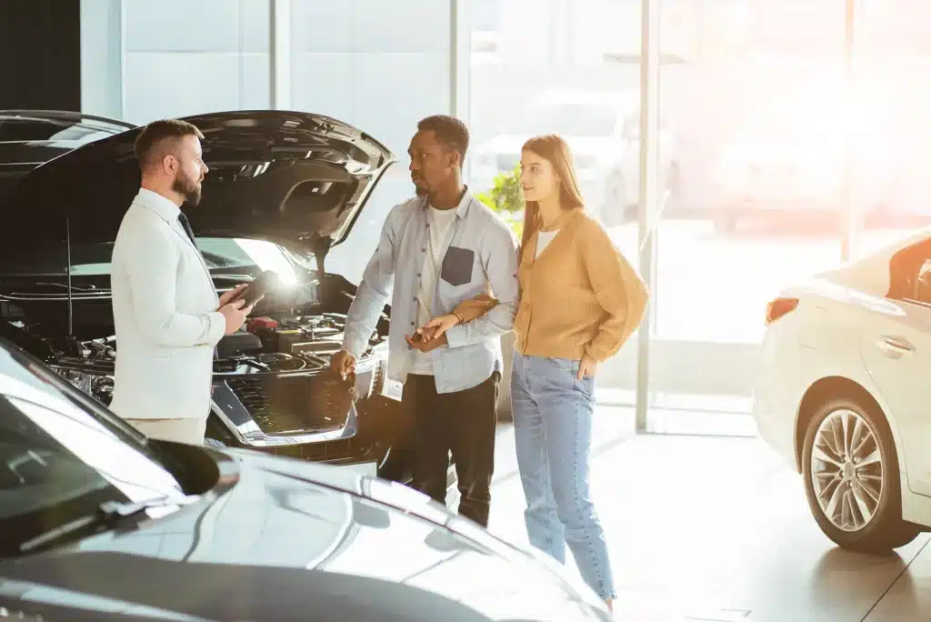 Couple speaking with car dealer beside vehicle with hood open in showroom